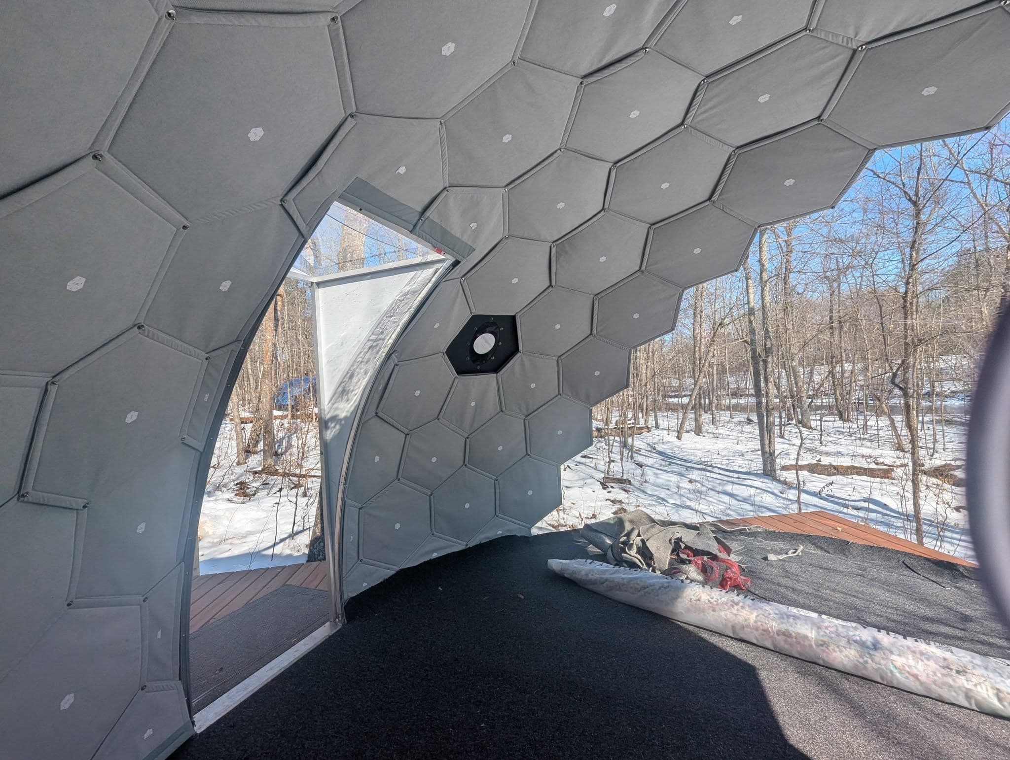 View from inside a geodesic dome looking out to a snowy forest valley